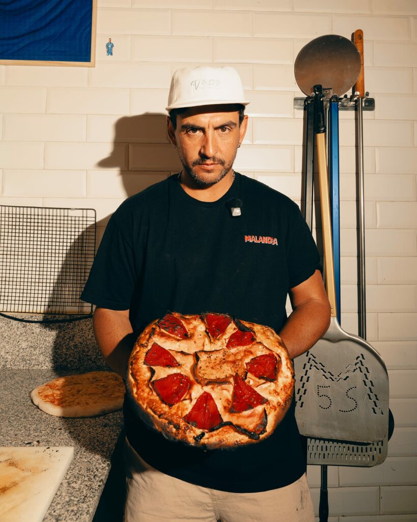 Pizzero de Malandra Pizza & Co sosteniendo una pizza en el obrador